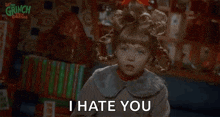 a little girl in a wig is standing in front of a bookshelf and saying `` i hate you '' .