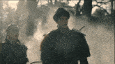 a man and a woman are standing in a forest with smoke coming out of the trees