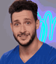 a man with a beard wearing a blue scrub top looks at the camera