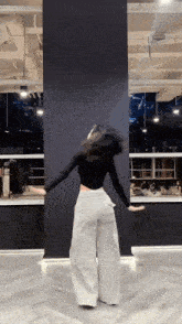 a woman in a black top and wide leg pants is dancing in a dance studio .