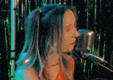 a woman is singing into a microphone in front of a green curtain
