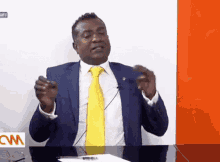 a man in a blue suit and yellow tie is sitting at a desk with a cnn logo in the background