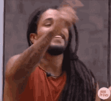 a man with dreadlocks and a beard is making a funny face while holding his hand to his face .