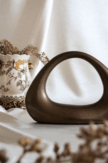 a white vase with gold flowers sits next to a brown vase with a handle