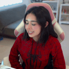 a woman wearing a red spider man hoodie sits in a pink chair