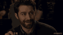 a man with a beard is smiling while holding a glass of wine