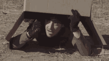 a man is hiding under a cardboard box
