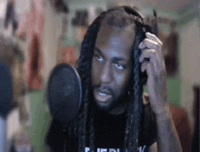 a man with long dreadlocks is standing in front of a microphone .