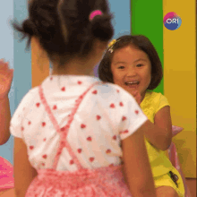 two little girls are waving at each other in front of a sign that says ori on it