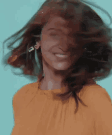 a woman in a yellow shirt is smiling while her hair blows in the wind .