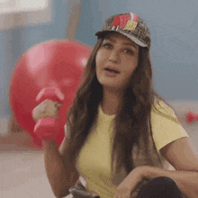 a woman is lifting a dumbbell in a gym while wearing a hat .