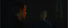 a man is looking at his reflection in a mirror in a dark room .