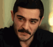 a close up of a man 's face with a mustache wearing a black shirt