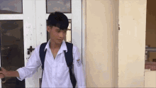 a young man with a backpack is standing in front of a white door .