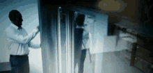 a man in a white shirt is opening a refrigerator door .
