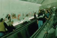 a group of people riding an escalator with graffiti on the wall