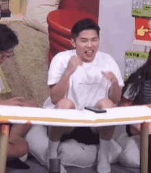a man in a white shirt is sitting at a table with a cell phone