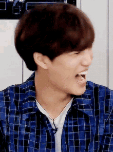 a young man wearing a blue plaid shirt is making a funny face