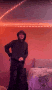 a man in a hoodie is dancing in a room with purple lights on the wall .