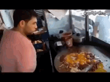 a man in a pink shirt is standing in front of a large plate of food .