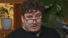 a man wearing glasses is sitting in front of a microphone with a mug that says budget