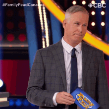 a man in a suit and tie holds a family feud sign