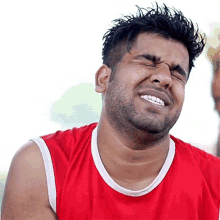 a man wearing a red shirt is laughing with his eyes closed