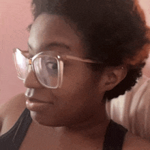 a woman wearing glasses and a black tank top looks to the side