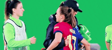 two female soccer players are hugging each other on a green screen . one of the players has the number 17 on her jersey .