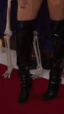 a woman wearing black over the knee boots is standing next to a skeleton .