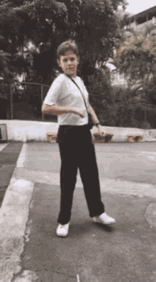 a young boy in a white shirt and black pants is dancing on a sidewalk .