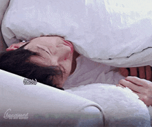 a person is sleeping on a couch with a white blanket on their head