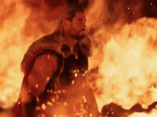 a man in a fur cape stands in front of a large fire