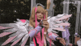 a woman in a pink and silver angel costume is standing in front of a building