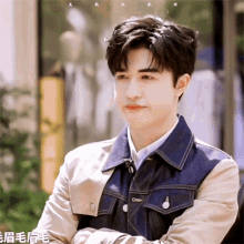 a young man in a denim jacket stands with his arms crossed and looks at the camera