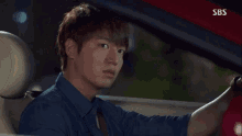 a man in a blue shirt is driving a red car with sbs written on the side of it