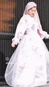 a woman wearing a white dress and a pink hijab is dancing