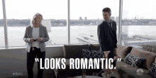 a man and a woman are standing in front of a window with the words " looks romantic " on the bottom