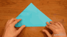 a person is folding a piece of blue paper into a triangle and the words made in animotica are visible