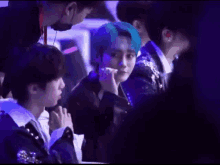 a group of young men are sitting at a table in a dark room . one of the men has blue hair .