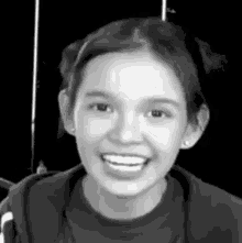a black and white photo of a young girl smiling in a room .