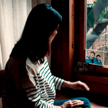 a woman sits in front of a window with a picture of a family on the window sill behind her