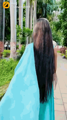 a woman in a blue dress is walking down a sidewalk with trees in the background