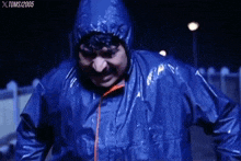a man in a blue raincoat with a hood is standing in the rain at night .