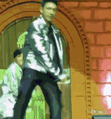 a man in a white jacket is dancing in front of a red wall