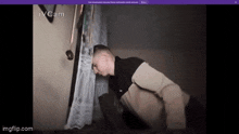 a man is kneeling down in front of a window with his head on the curtain .
