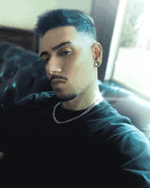a man wearing a black shirt and a silver chain around his neck looks at the camera