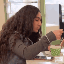 a woman sitting at a table with a phone and a cup of coffee with a bravo logo on the bottom