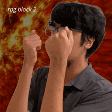 a man wearing glasses holds his fist up in front of a fire background with the words rpg block 2 below him