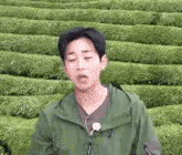 a man wearing a green jacket is standing in front of a field of green plants .